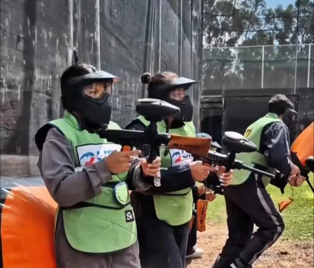 Cuatro jugadores con máscara y chaleco verde avanzan en formación durante una partida de paintball