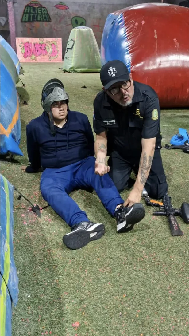 Paramédico uniformado revisa el tobillo de un jugador sentado en el césped de la cancha, junto a los búnkeres inflables